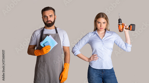 Gender stereotypes and non female profession. Serious man in apron and rubber gloves holding sponges and woman holding a drill