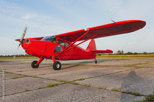 A vintage red small plane Stinson is preparing to take off on a private concrete runway.