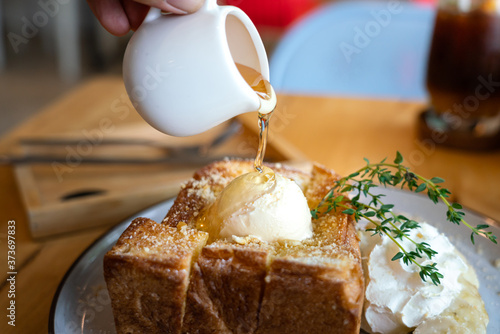 Action of people hand is topping honey sweet on the vanilla ice cream of Honey toast sweet menu. Selective focus at the honey surface.