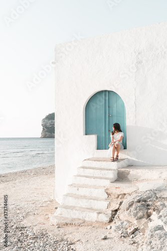 Chica sentada en puerta de madera azul en cala Portixol en Jávea frente al mar mediterráneo