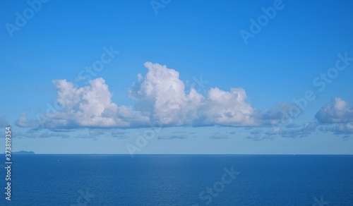 View of a calm blue sea with white fluffy clouds and clear blue sky on a sunny day in early morning .