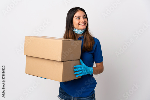 Young delivery woman protecting from the coronavirus with a mask isolated on white background looking up while smiling