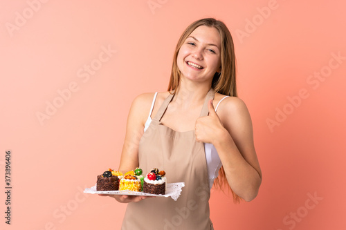 Pastry Ukrainian chef holding a muffins isolated on pink background giving a thumbs up gesture