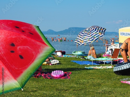 Balatonmáriafürdő, Hungary - July 29, 2020: Colorful umbrellas, sunbathing and bathing people on the beach of the lake Balaton, Hungary in hot July day