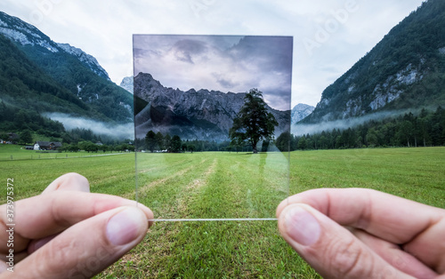 Professional photographer holding ND Gradient Filter glass appreciating an effect. Logar valley, Slovenia.