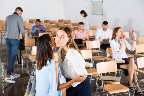 Two girls friendly greeting each other with kiss in auditorium before training course..