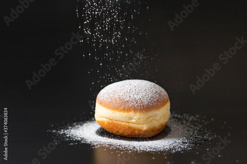 doughnut with powdered sugar infront of a black background