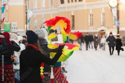 Girls in winter jackets dance on a snowy street with fans. Hare Krishna sectarians