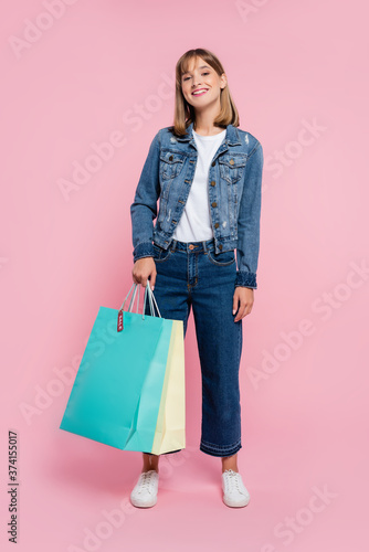 Young woman holding shopping bags with price tag and looking at camera on pink background