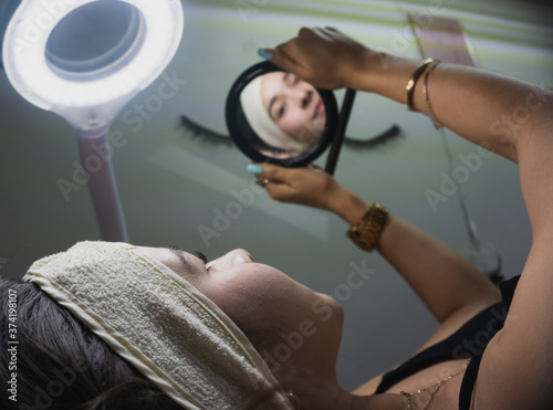 Young woman looks in a mirror after receiving facial treatment