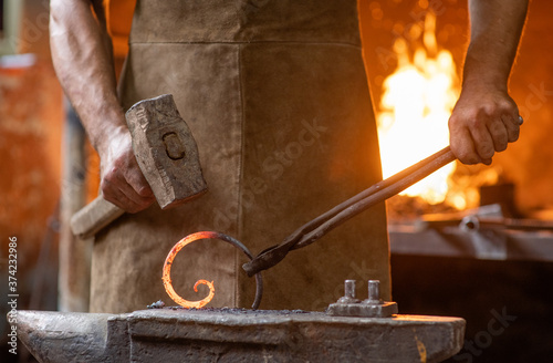 Close up blacksmith is processing a hot metal object of a spiral shape at anvil in a workshop