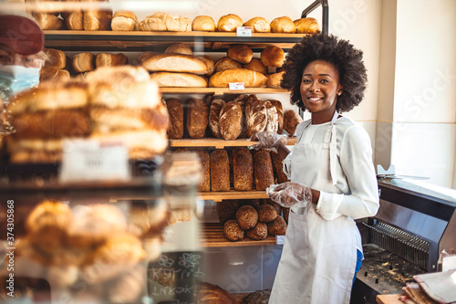She will have you coming back for more. Gorgeous young woman in her bakery smiling cheerfully to the camera. Smiling young woman selling bread in the bakery. Happy african baker woman