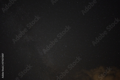 Milky way and many stars in front of a black blue night sky, orange colored cloud in the foreground. Germany.