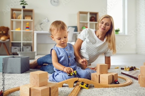 Young babysitter and little child playing with wooden blocks in cozy nursery room