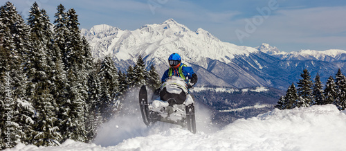 Pro snowmobiler makes a turn and lets a flurry of snow spray from under the caterpillar. sports snowmobile in the mountains. bright skidoo motorbike and suit without brands. Winter fun moto extreme