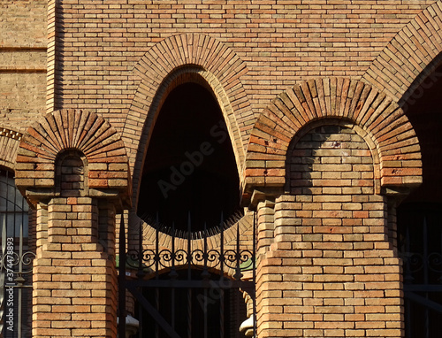 Detail of Revival metallic and brick fence and wall with catenary arch. Old city center of Tarragona. Catalonia. Spain. 