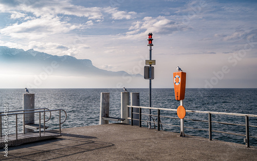 View on the Lake Geneva (Lac Leman) and Swiss Alps from a ferry pier in the city of Vevey, Switzerland. The sign "Fishing prohibited" is on the signal column