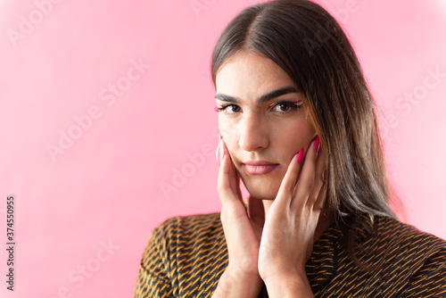 Studio portrait with pink background of a young man with make-up and colorful long nails.