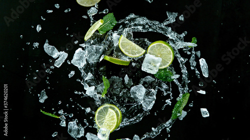 Fresh ripe limes with ice cubes flying on a black background. Freeze motion.