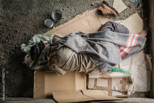 Old homeless man wearing sweater and blanket sleeping on cardboard seeking help because hungry and food beggar from people walking pass on street. Poor man homeless and depression concept.