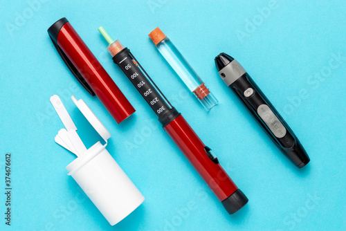Diabetic set of lancet with spare needles, strips, box of spare strips, pen injector, spare insulin and pen needles on a blue background