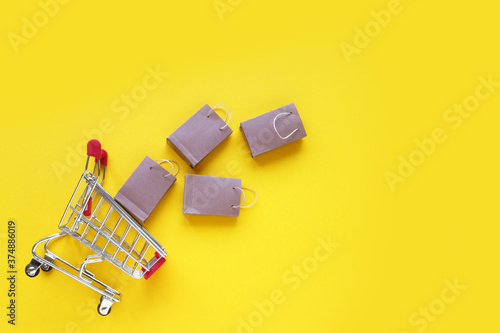 Mini shopping cart with small craft bags on the yellow background.