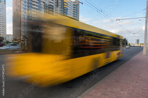 The movement of a blurred bus along the avenue in the daytime.
