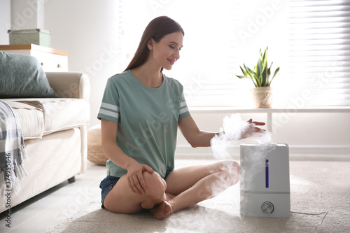 Woman near modern air humidifier at home