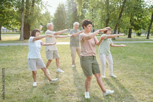 Group of focused senior people and their coach gesturing hands and doing qigong exercise in park