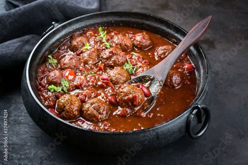 Traditional slow cooked American Tex Mex meatballs chili with mincemeat and beans in a spicy sauce offered as close-up in a design cast-iron roasting dish 