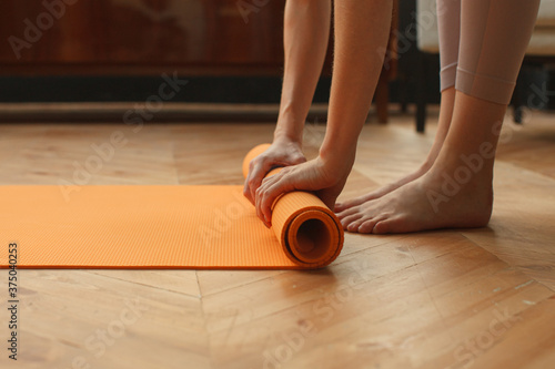 female hands unrolling yoga mat in home on parquet floor, preparing for yoga practice, detail shot