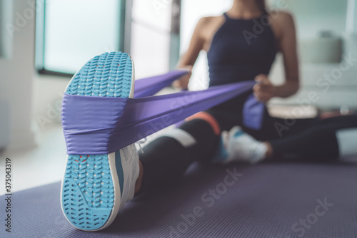 Resistance band exercise at home. Woman doing pilates workout using elastic strap pulling with arms for shoulder training on yoga mat indoors.