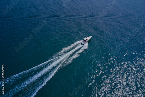 Drone view of a yacht sailing across the blue clear waters. Top view of a white yacht sailing in the blue sea. Aerial view luxury motor yacht.
