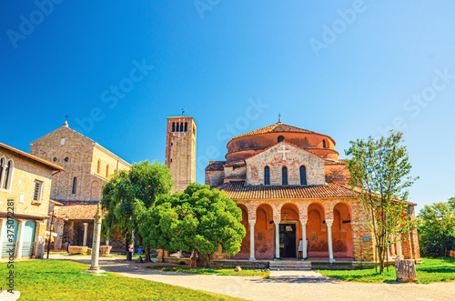 Church of Santa Fosca building on Torcello island, Cathedral of Santa Maria Assunta with bell tower campanile, blue clear sky background. Venetian Lagoon, Veneto Region, Northern Italy.