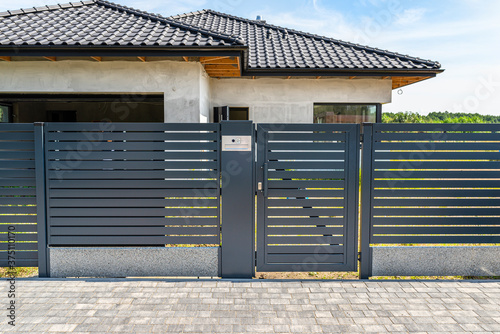 Modern panel fencing in anthacite color, visible wicket with videophone and a house in the background.