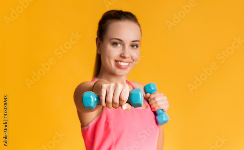 Sporty Girl Doing Dumbbell Boxing Workout Over Yellow Studio Background