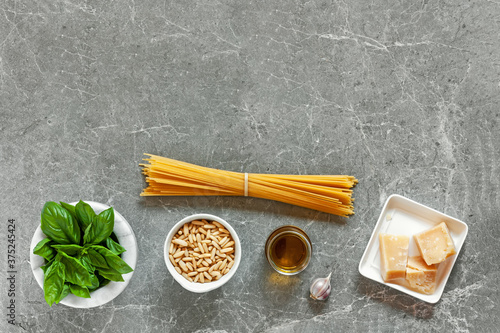 Pasta with pesto ingredients. Top view of spaghetti, basil, pine nuts, garlic, parmesan and olive oil on gray stone background