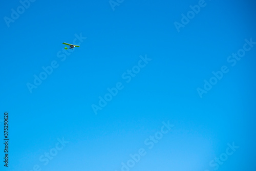 A small green plane flies against a bright blue cloudless sky.