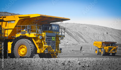 Spot color trucks, two large yellow truck used in a modern coal mine in Queensland, Australia. Trucks transport coal from open cast mine. Fossil fuel industry, Environmental challenge. Logos removed.