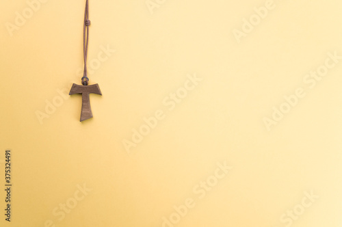 Closeup of a wooden tau cross necklace isolated on a yellow background