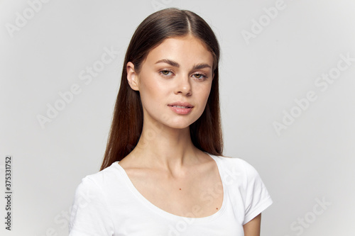 Beautiful brunette girl in a white t-shirt looks ahead on an isolated background close-up 