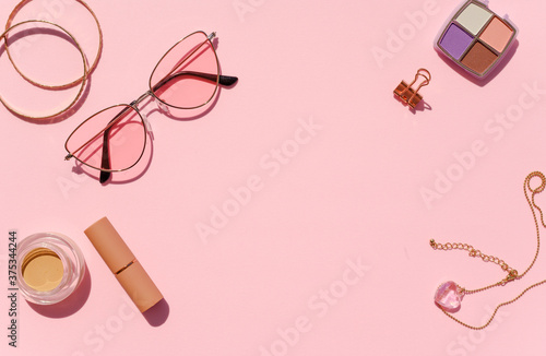 Feminine desk frame mockup. Top view cosmetics, jewelry and sunglasses on a pink background. Space for promo