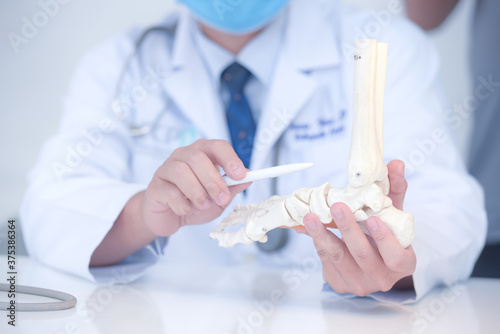 Asian orthopedic doctor in his office with a patient and a model of the foot