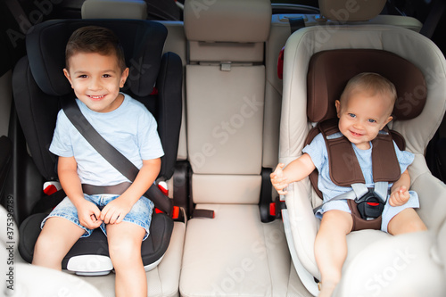 Kids, little girl with her brother sitting together in car seat locked with safety belts