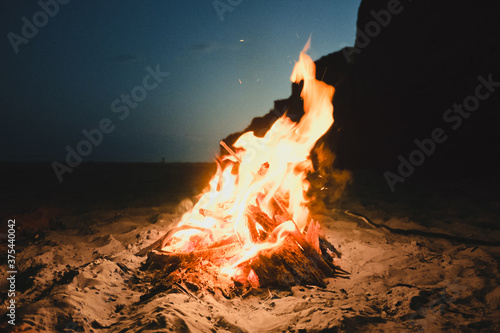 Fire burning on the sand coast on a sunny summer evening. Small fire burns inside a fireplace on the empty beach. Photo with Film and Grain Effect