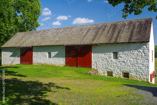 Colonial barn at the Hopewell Furnace National Historic Site in Pennsylvania. Massive, elegant whitewashed stone with red doors and ventilation windows. Notice the rat tail hinges on the doors. Full