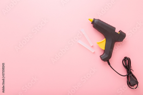Black glue gun with plastic sticks on light pink background. Pastel color. Closeup. Empty place for text. Top down view.