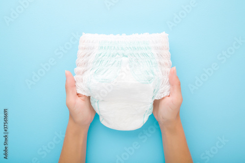 Young mother hands holding white baby diaper pants on light blue table background. Pastel color. Closeup. Point of view shot. Top down view.