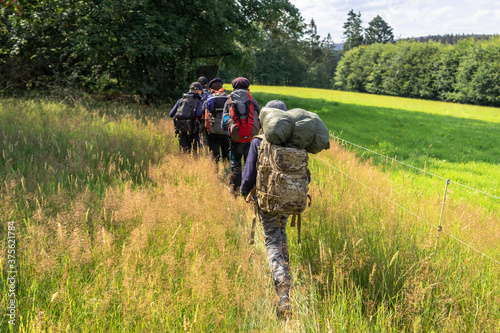 Scouts or tourists go with big backpacks on the green forest trail on sunny summer day. Active healthy lifestyle people with rucksacks. Hiking Trekking Scouting. Green forest background.