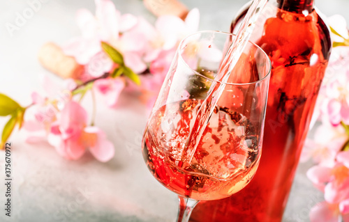 Rose wine pouring out of the bottle, gray bakcground, pink flowers. Rosado, rosato or blush wine tasting in wineshop, bar concept. Copy Space